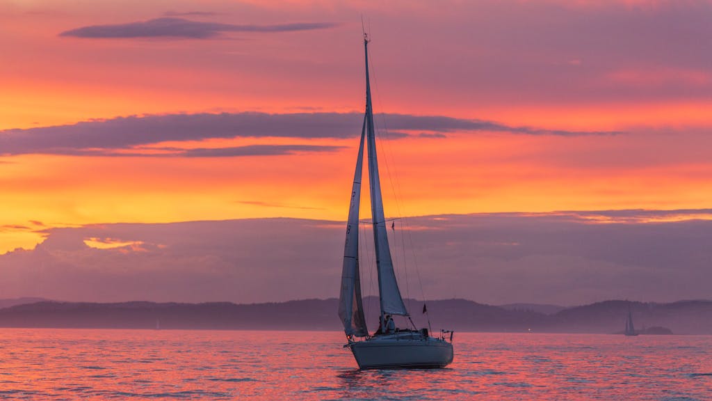 A serene sailboat silhouette against a vibrant sunset sky in Norway.